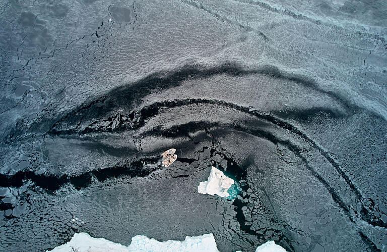 Aerial image showing two small fishing boats breaking a path through sea ice