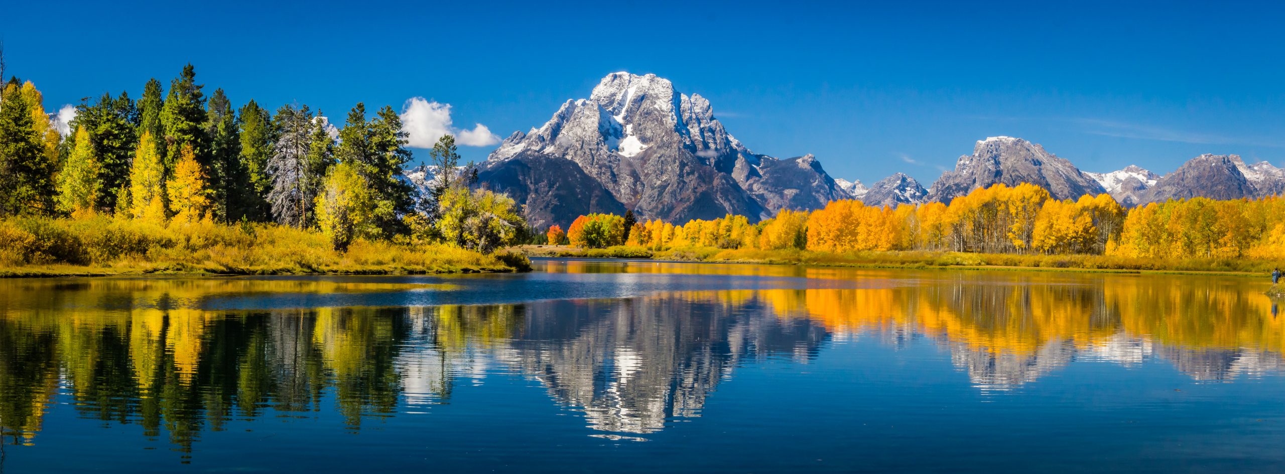 A snow mountain surrounded by trees in autumn foliage, reflected in a lake